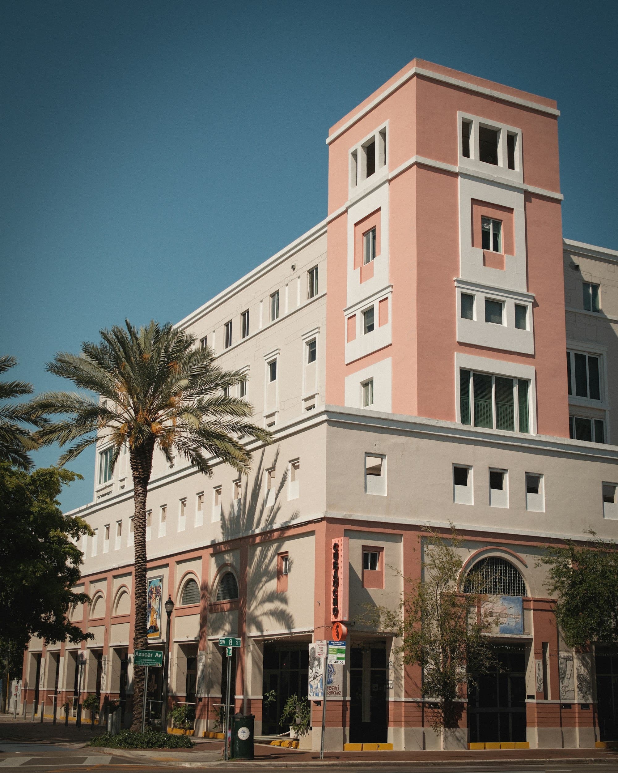 A pink and white building in Miami against a blue sky, palm trees below